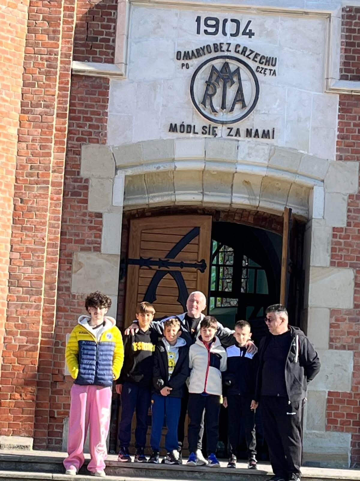 Grup de copii și adulți fotografiați în fața unei clădiri istorice din cărămidă roșie
